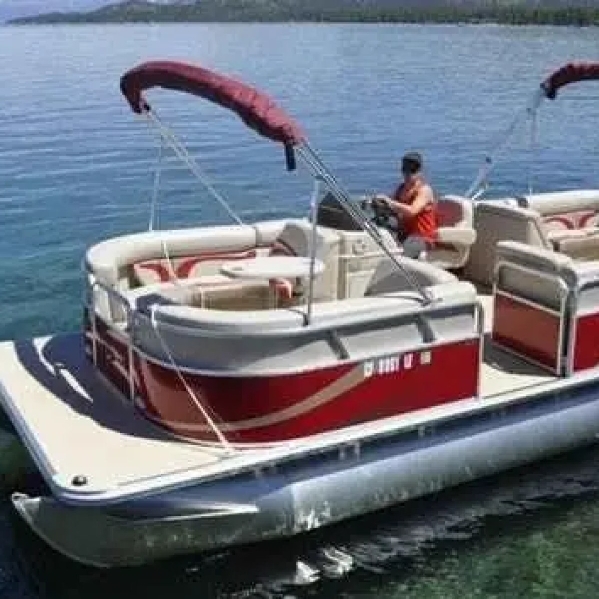 Pontoon boat with red canopy on clear blue lake water.