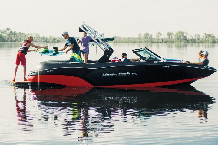 People on a boat assist a wakeboarder on a lake.