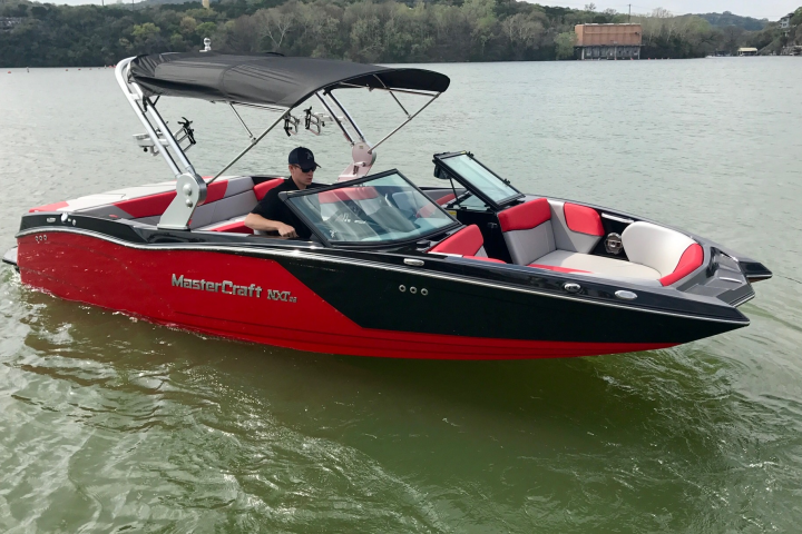 Red and black motorboat on a lake, with a man steering.