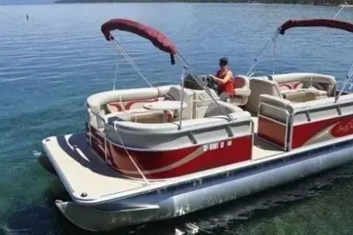 Red and white pontoon boat with person steering on a lake.