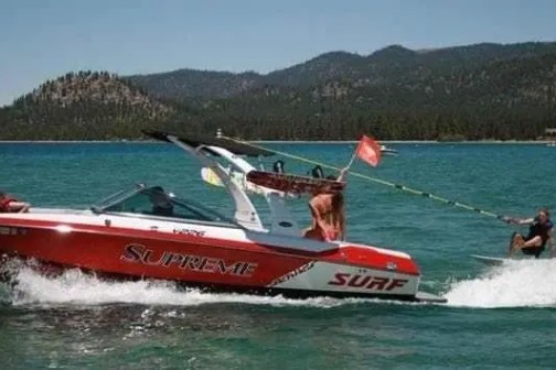 Red speedboat towing a water skier on a lake with mountains in background.